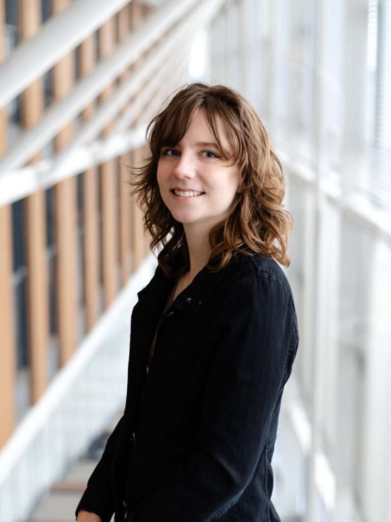 Dr. Kress stands in front of a modern building. She is wearing a black jacket and has curly dark blonde hair.